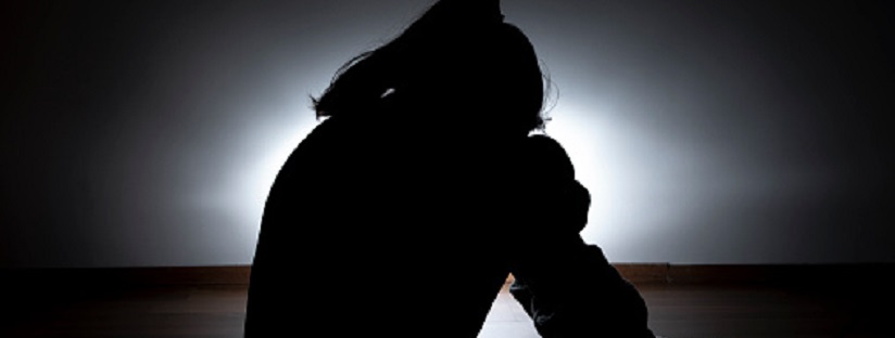 child with head resting on knees in dark room