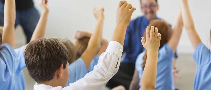 School children in school uniform with hands up ready to answer a question from the teacher