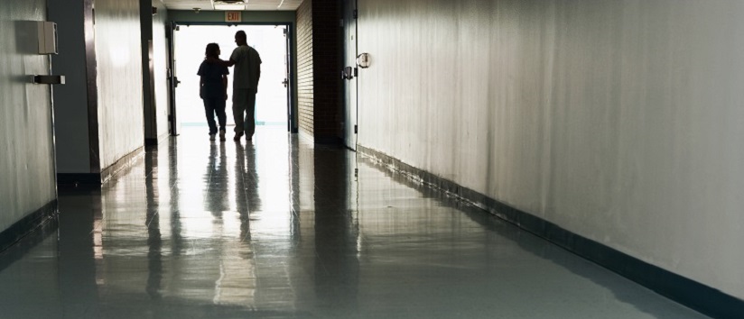 Two people standing at end of corridor in hospital