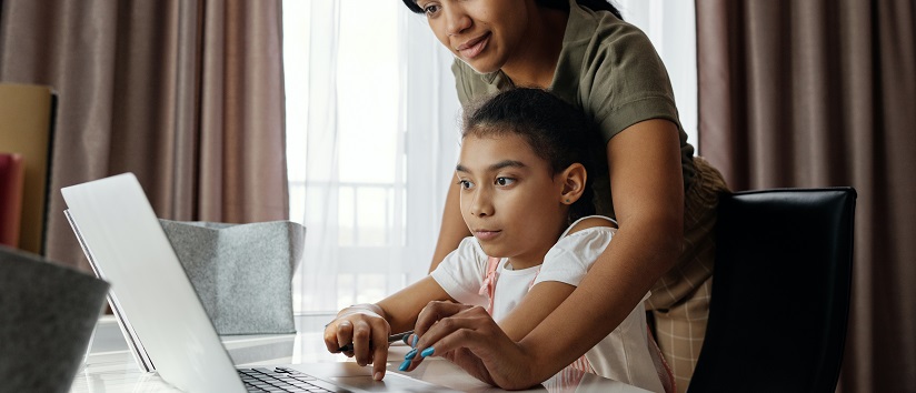 Child using laptop with help from parent