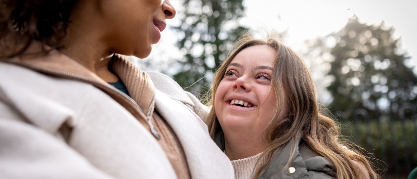 Close-up of a woman with her sister who has Down syndrome smiling at each other face to face. They are both wearing warm clothing on a cold winter morning. The park is located in Gateshead.